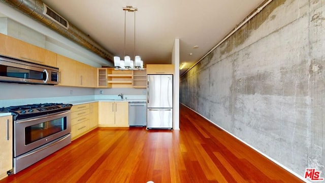 kitchen featuring appliances with stainless steel finishes, light brown cabinets, decorative light fixtures, and hardwood / wood-style floors