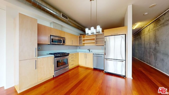 kitchen featuring stainless steel appliances, sink, light brown cabinets, decorative light fixtures, and hardwood / wood-style floors