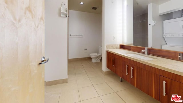 bathroom with tile patterned floors, stacked washer and dryer, vanity, and toilet