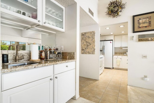 bar featuring light stone counters, white refrigerator with ice dispenser, sink, and white cabinetry