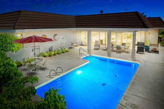 pool at night with a grill and a patio area