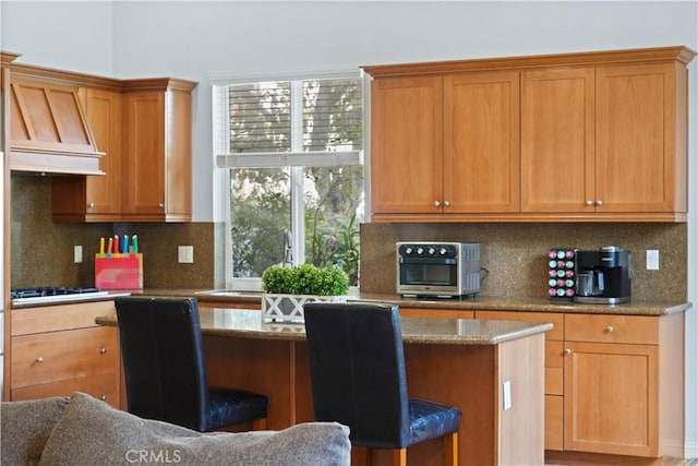 kitchen featuring tasteful backsplash, black gas cooktop, premium range hood, and a breakfast bar