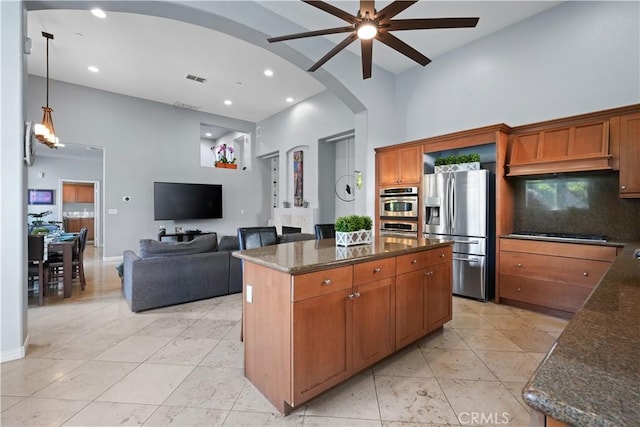 kitchen with arched walkways, a high ceiling, appliances with stainless steel finishes, backsplash, and dark stone counters