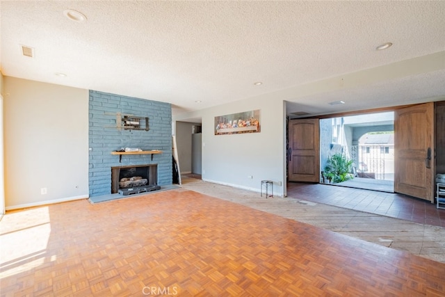 unfurnished living room with light parquet floors, a textured ceiling, and a brick fireplace