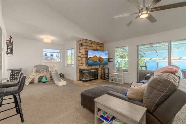 carpeted living room featuring ceiling fan, plenty of natural light, a stone fireplace, and vaulted ceiling