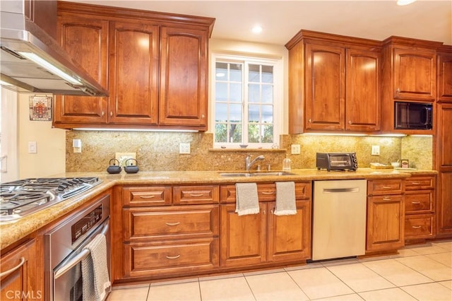 kitchen featuring light tile patterned floors, appliances with stainless steel finishes, wall chimney exhaust hood, light stone counters, and sink