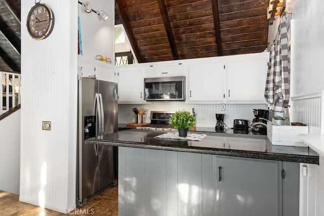 kitchen featuring lofted ceiling with beams, wood ceiling, stainless steel appliances, dark stone countertops, and white cabinetry