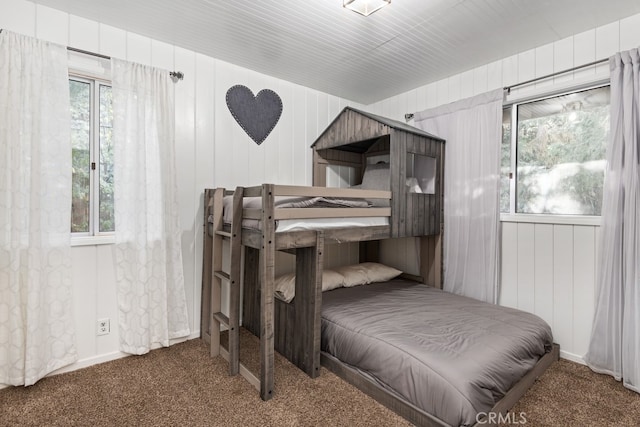 bedroom featuring wooden walls, dark colored carpet, and multiple windows