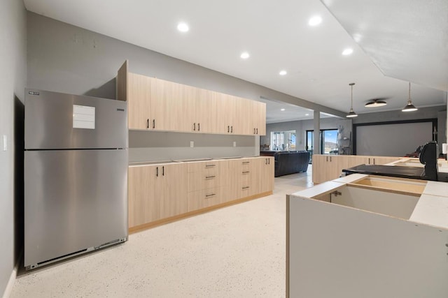 kitchen featuring stainless steel fridge, light brown cabinetry, and decorative light fixtures