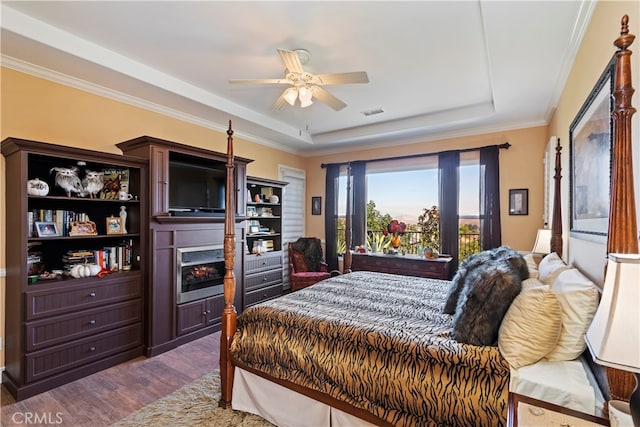 bedroom with crown molding, a tray ceiling, dark hardwood / wood-style flooring, and ceiling fan