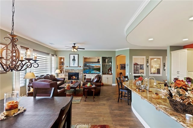 dining area featuring ceiling fan, sink, ornamental molding, a stone fireplace, and dark hardwood / wood-style floors