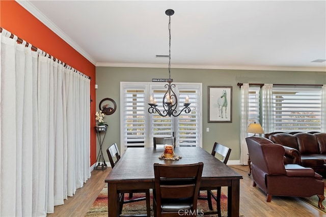 dining space with a healthy amount of sunlight, crown molding, an inviting chandelier, and light hardwood / wood-style floors