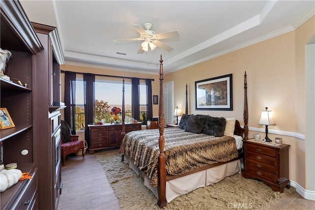 bedroom with ornamental molding, a tray ceiling, light wood-type flooring, and ceiling fan