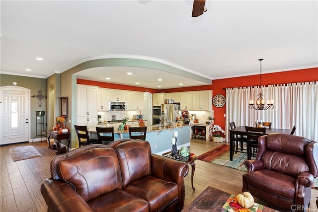 living room with ornamental molding, ceiling fan with notable chandelier, and light hardwood / wood-style flooring