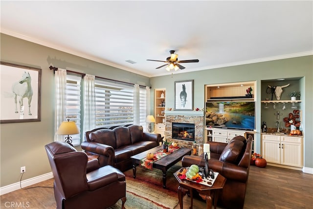 living room featuring ceiling fan, a stone fireplace, dark hardwood / wood-style floors, indoor wet bar, and crown molding