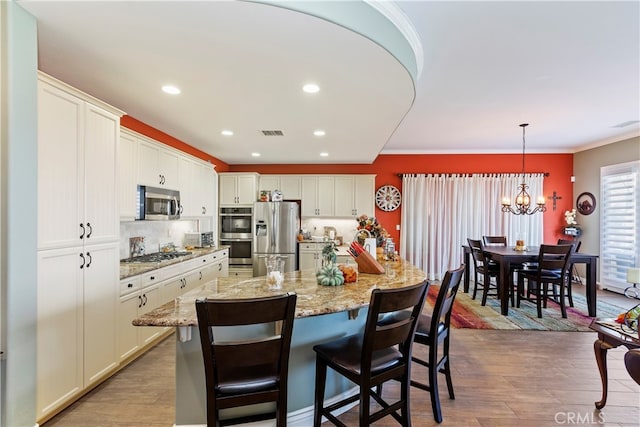 kitchen featuring light wood-type flooring, decorative light fixtures, stainless steel appliances, an island with sink, and white cabinets