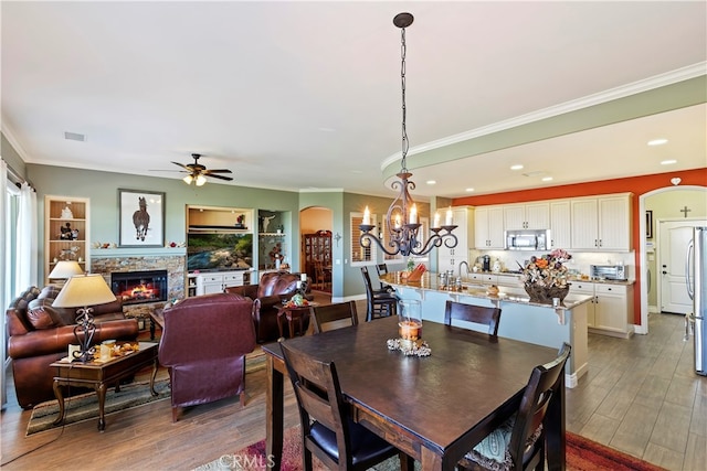 dining space featuring ceiling fan with notable chandelier, dark hardwood / wood-style floors, crown molding, and a stone fireplace