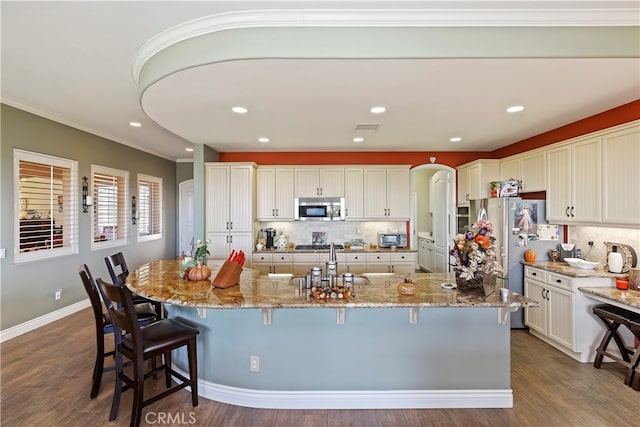 kitchen featuring stainless steel appliances, an island with sink, dark wood-type flooring, and a kitchen bar