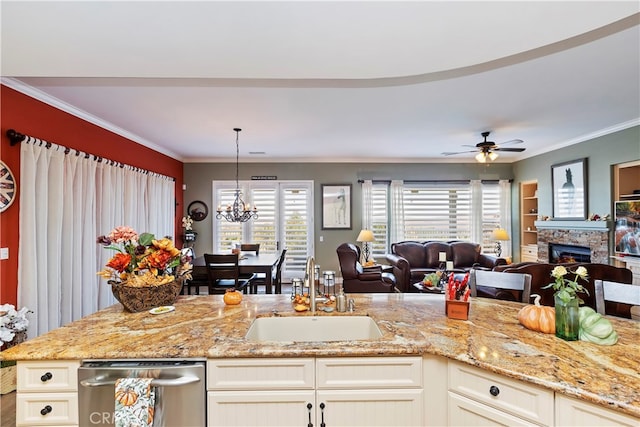 kitchen with light stone countertops, sink, a stone fireplace, ceiling fan with notable chandelier, and crown molding