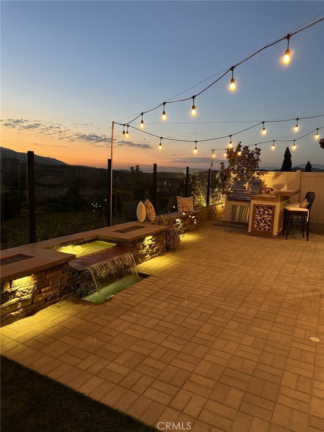 patio terrace at dusk featuring pool water feature, a grill, area for grilling, and an outdoor bar