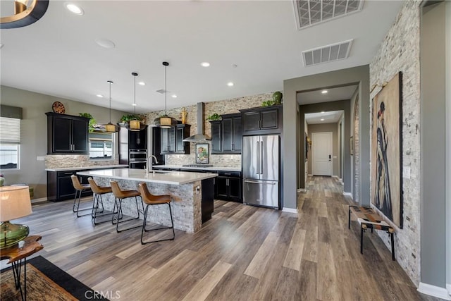 kitchen featuring pendant lighting, wall chimney exhaust hood, stainless steel appliances, and tasteful backsplash