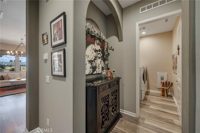 corridor with washer and clothes dryer, light hardwood / wood-style floors, and a notable chandelier