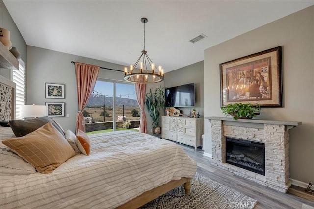 bedroom with hardwood / wood-style floors, a stone fireplace, and a chandelier