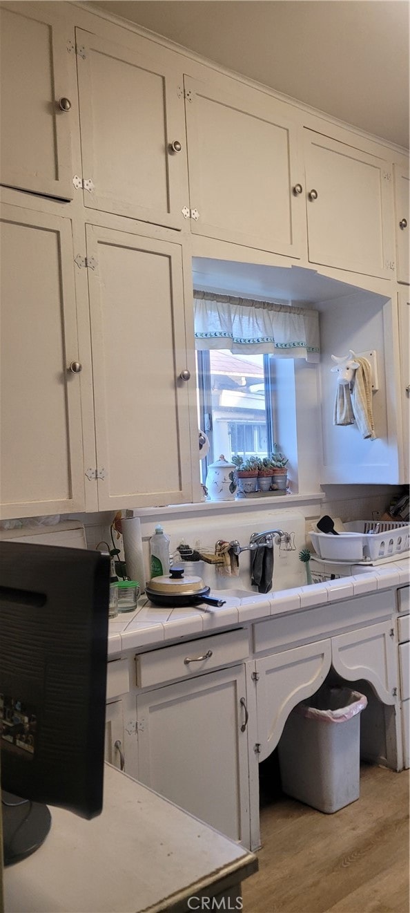 kitchen featuring tile counters, light hardwood / wood-style flooring, and white cabinets