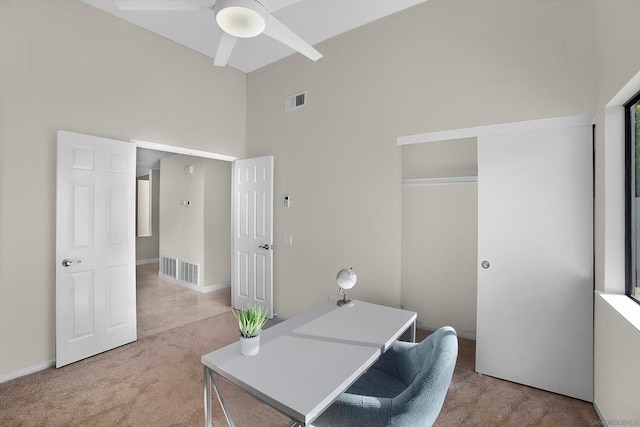 home office with a towering ceiling, ceiling fan, and light colored carpet