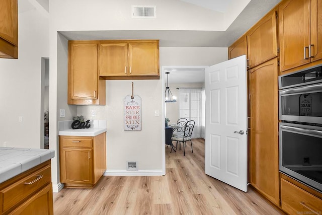 kitchen with lofted ceiling, hanging light fixtures, double oven, tile countertops, and light wood-type flooring