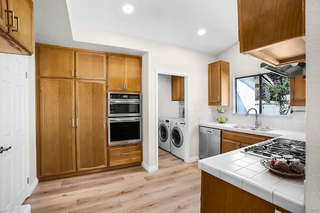 kitchen featuring sink, light hardwood / wood-style flooring, stainless steel appliances, tile countertops, and independent washer and dryer