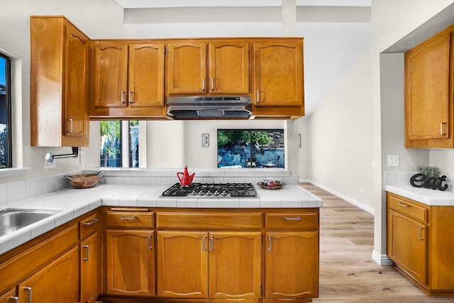 kitchen featuring light hardwood / wood-style flooring, tile countertops, kitchen peninsula, and stainless steel gas cooktop