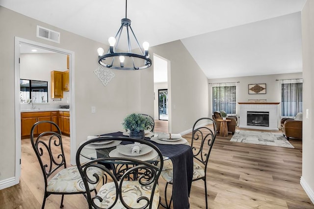 dining space with light hardwood / wood-style floors, lofted ceiling, a chandelier, and a brick fireplace