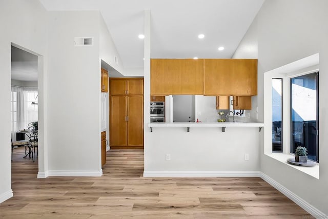 kitchen featuring light wood-type flooring, kitchen peninsula, a kitchen bar, high vaulted ceiling, and double oven