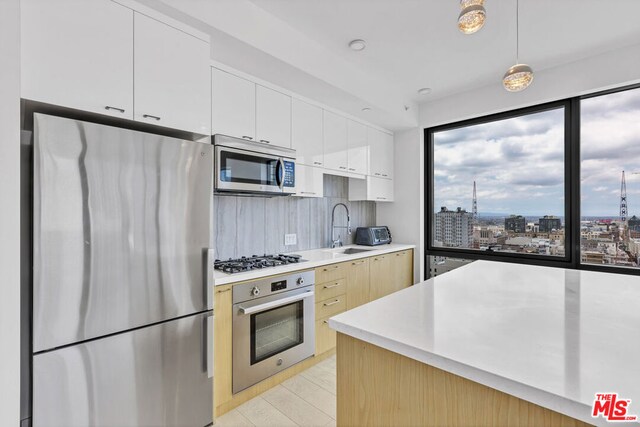 kitchen with sink, hanging light fixtures, decorative backsplash, appliances with stainless steel finishes, and white cabinetry