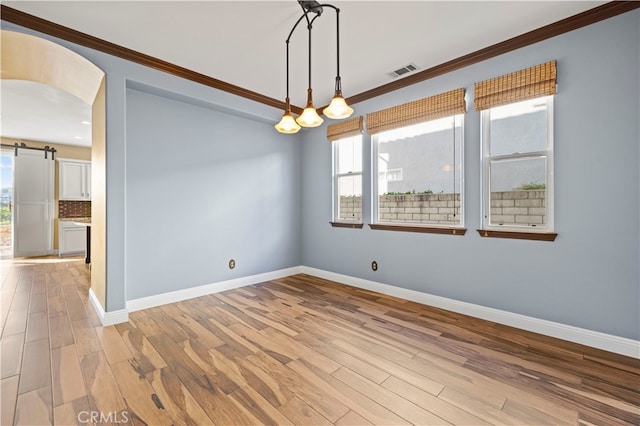 empty room featuring light wood-type flooring, a barn door, and ornamental molding