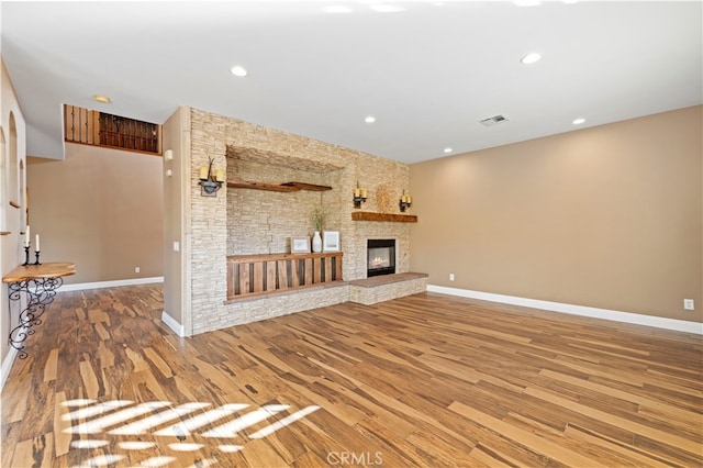 unfurnished living room featuring hardwood / wood-style floors and a stone fireplace