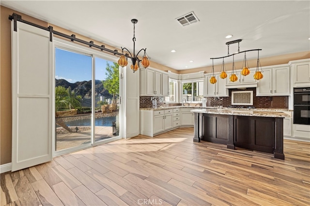 kitchen with double oven, a center island, light wood-type flooring, and decorative light fixtures