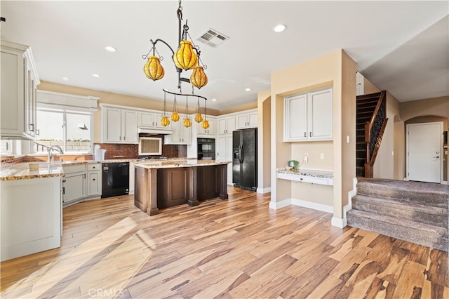 kitchen featuring a kitchen island, decorative light fixtures, black appliances, light stone countertops, and light hardwood / wood-style floors