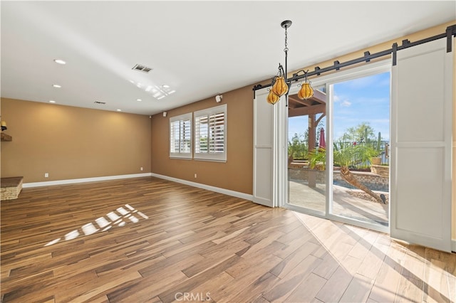 unfurnished dining area with a barn door and hardwood / wood-style floors