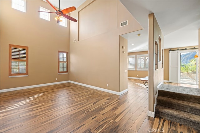 living room with a barn door, wood-type flooring, a towering ceiling, and ceiling fan