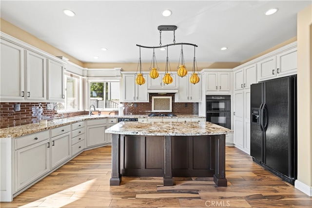 kitchen with light wood-type flooring, decorative light fixtures, black appliances, a center island, and light stone countertops