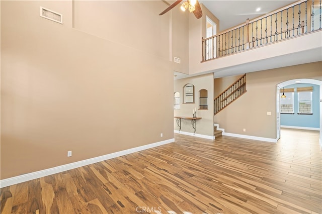 unfurnished living room with a towering ceiling, wood-type flooring, and ceiling fan