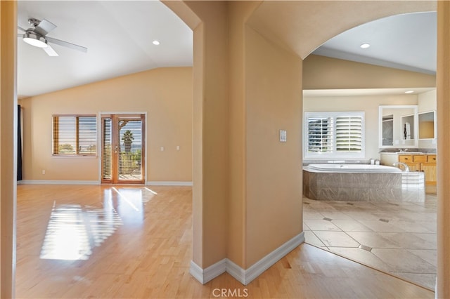 hallway with lofted ceiling, sink, light hardwood / wood-style flooring, and plenty of natural light