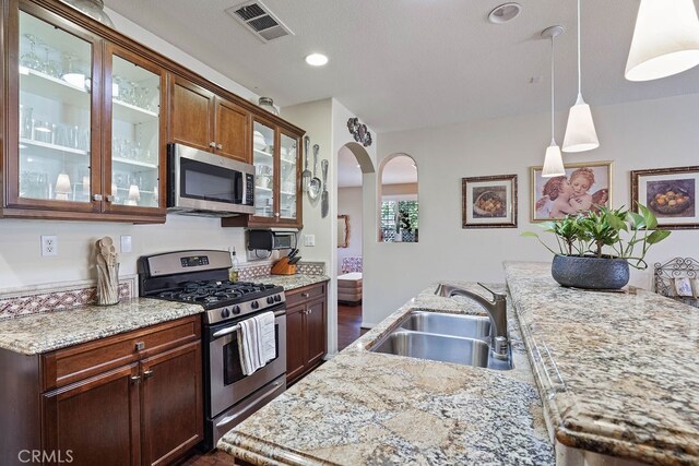 kitchen featuring light stone counters, dark wood-type flooring, sink, hanging light fixtures, and appliances with stainless steel finishes