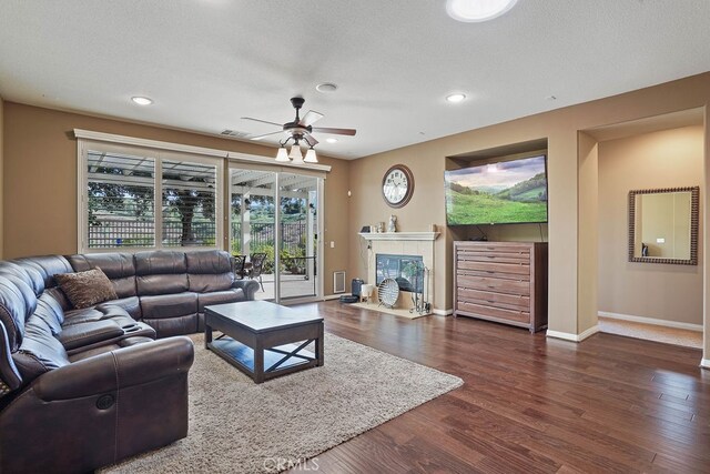 living room featuring a tiled fireplace, dark hardwood / wood-style flooring, a textured ceiling, and ceiling fan