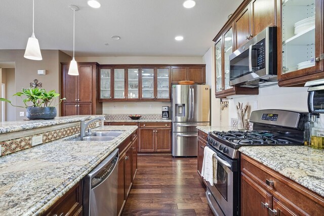 kitchen with light stone countertops, stainless steel appliances, sink, dark hardwood / wood-style flooring, and decorative light fixtures