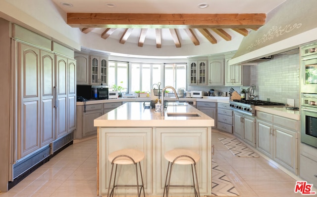 kitchen with a kitchen bar, sink, tasteful backsplash, a center island with sink, and stainless steel appliances