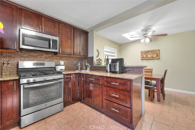 kitchen featuring light stone counters, decorative backsplash, stainless steel appliances, a skylight, and ceiling fan