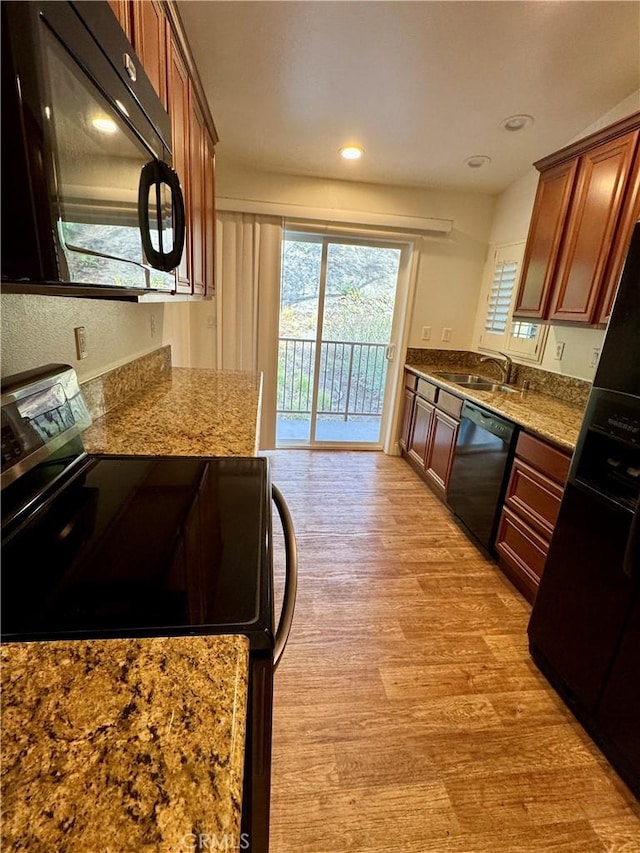 kitchen featuring light stone counters, a sink, light wood-style floors, black appliances, and brown cabinetry